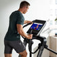 Man in dark teal t-shirt and black shorts using black NordicTrack FS14i elliptical with digital display screen in bright home