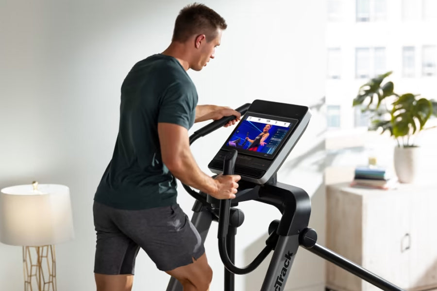Man in dark teal t-shirt and black shorts using black NordicTrack FS14i elliptical with digital display screen in bright home