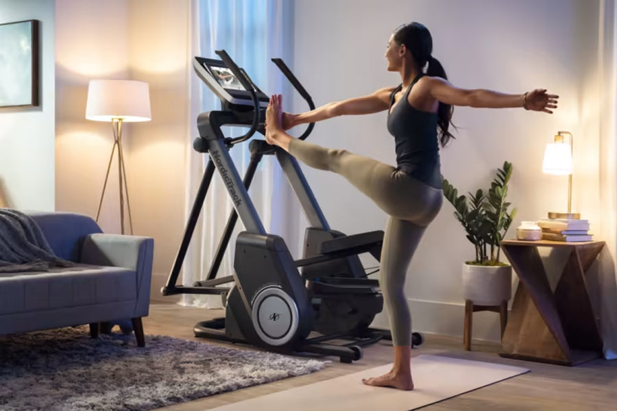 Woman using black NordicTrack elliptical machine with extended arms in modern living room setting