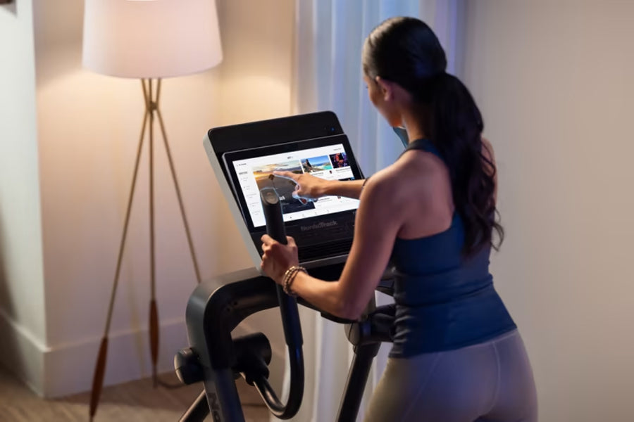 Woman using black NordicTrack elliptical with touchscreen display in home gym setting
