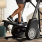 Black and gray elliptical machine with person wearing black shorts and sneakers exercising in home gym setting