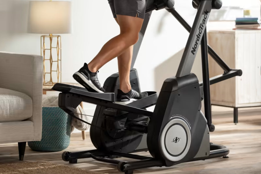 Black and gray elliptical machine with person wearing black shorts and sneakers exercising in home gym setting