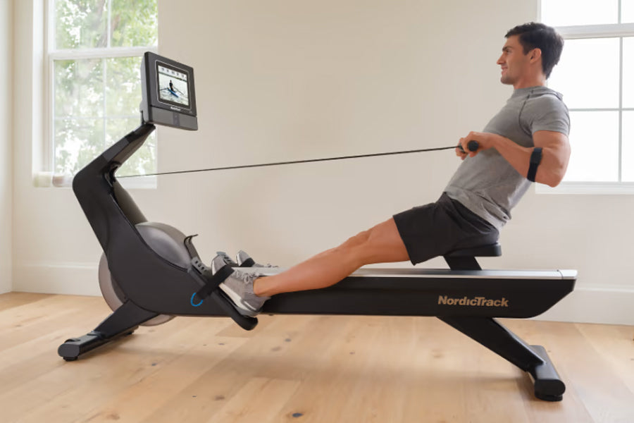 Man using black NordicTrack rowing machine with digital display in home gym setting