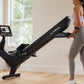 Woman in white sports bra and gray leggings using black NordicTrack rowing machine with digital display in bright home gym