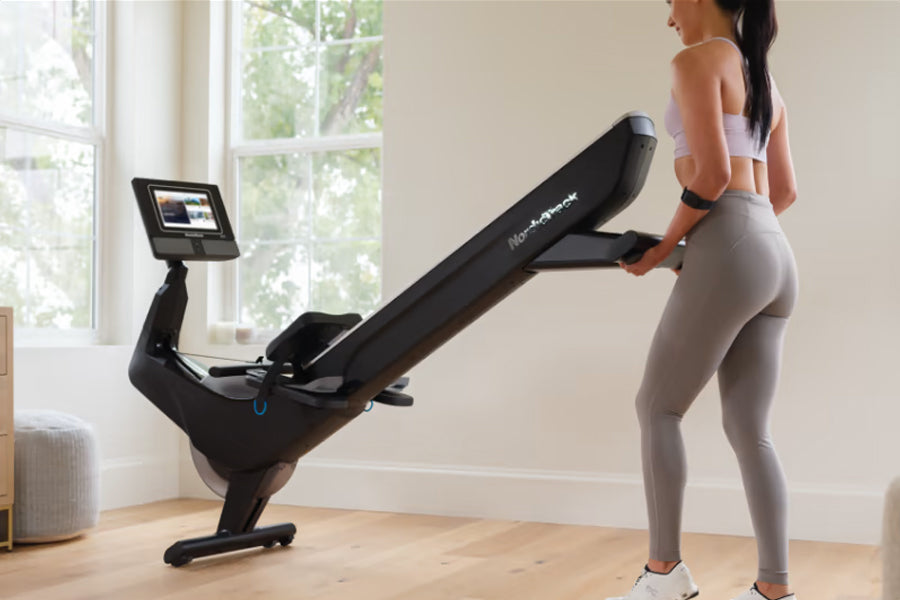 Woman in white sports bra and gray leggings using black NordicTrack rowing machine with digital display in bright home gym
