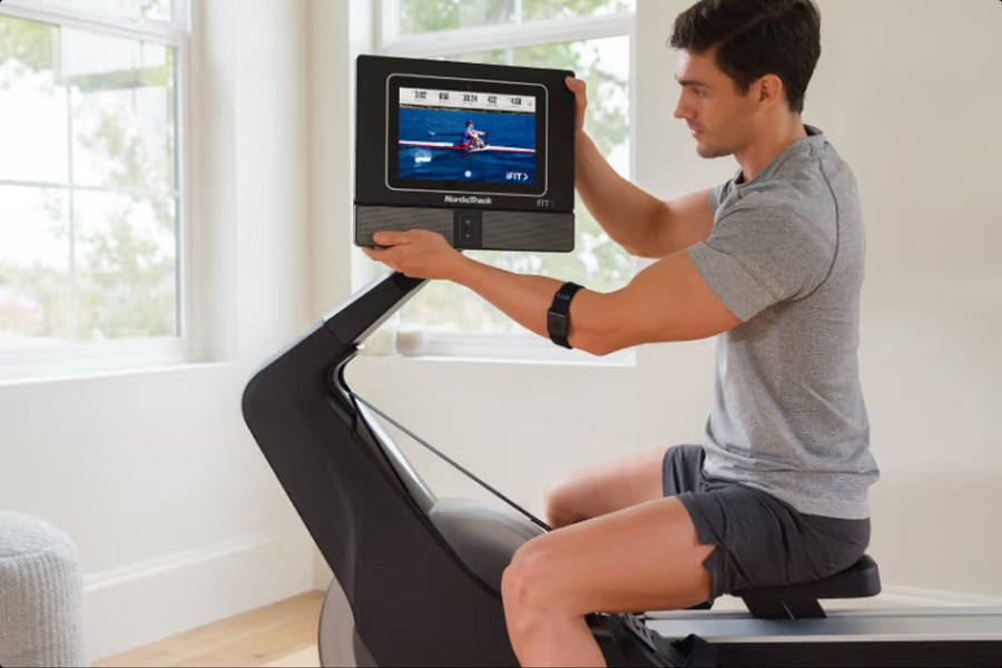 Man using NordicTrack RW700 rowing machine with digital display showing workout metrics in bright home setting