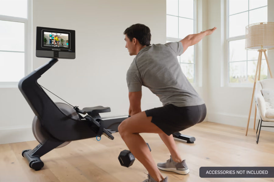 Man using black NordicTrack rowing machine with digital touchscreen display in bright room with windows