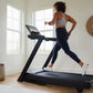 Woman running on black NordicTrack treadmill with touchscreen display in bright home gym with wooden shelving