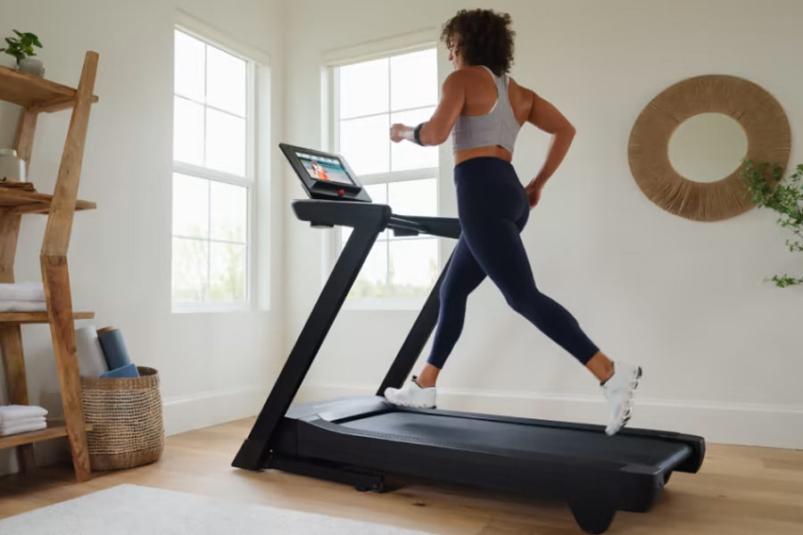 Woman running on black NordicTrack treadmill with touchscreen display in bright home gym with wooden shelving
