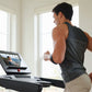 Man wearing black sleeveless tank top running on treadmill with digital display in bright room with windows