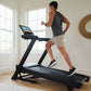 Man running on black NordicTrack treadmill with digital display in bright home gym with windows