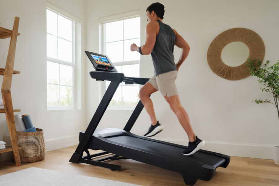 Man running on black NordicTrack treadmill with digital display in bright home gym with windows