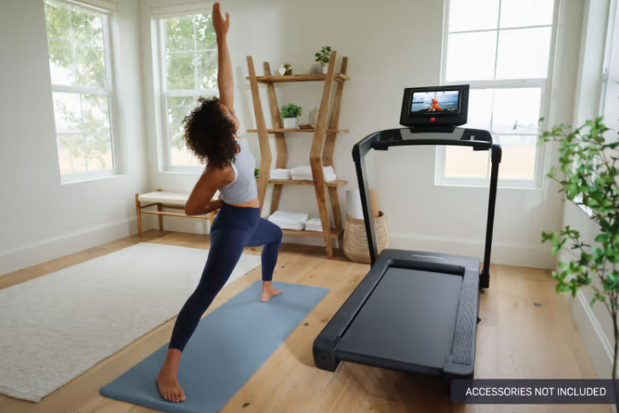 Black motorized treadmill with digital display, shown in home gym setting with woman exercising on blue mat