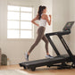 Woman running on black NordicTrack treadmill wearing white sports bra and beige leggings in bright home gym