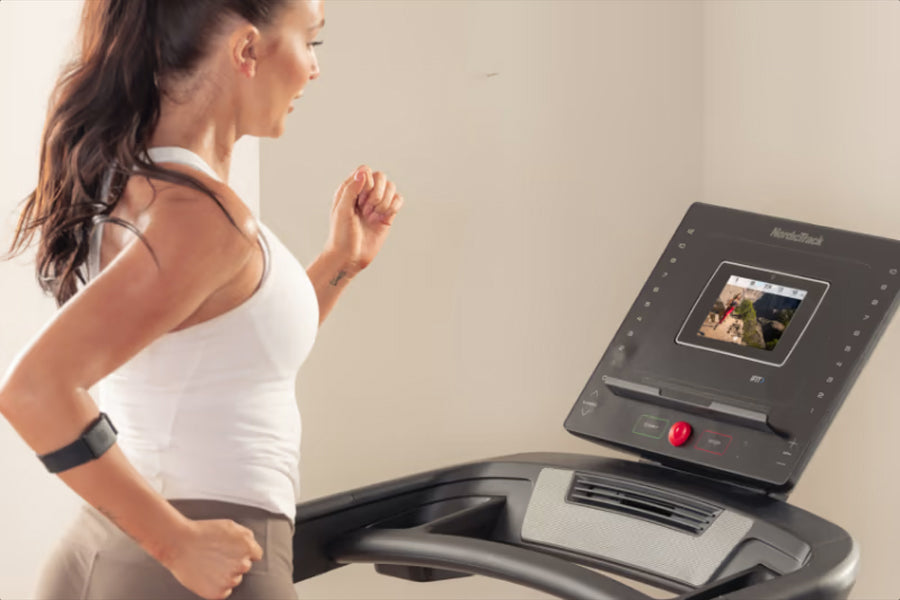 Woman in white tank top running on NordicTrack EXP 7i treadmill with black console display
