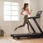 Woman running on black NordicTrack treadmill wearing white sports bra and brown leggings in bright home gym