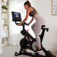 Woman exercising on black NordicTrack S10i stationary bike with touchscreen display in bright home gym setting
