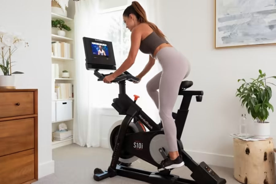 Woman exercising on black NordicTrack S10i stationary bike with touchscreen display in bright home gym setting