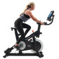 Woman on black NordicTrack S15i stationary bike with digital display, wearing black sports bra and leggings, on white backgro
