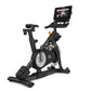 Black NordicTrack S15i indoor exercise bike with attached touchscreen display showing workout content, viewed from side on wh