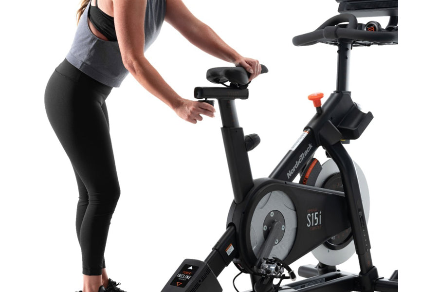 Woman in black leggings and gray tank top using NordicTrack S15i stationary exercise bike with black frame and gray flywheel 