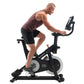 Man in burgundy tank top and black shorts riding black NordicTrack S15i stationary bike with digital display on white backgro
