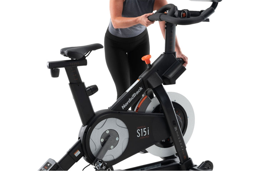 Person using black and gray NordicTrack S15i stationary bike with orange accents and digital display