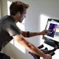 Man wearing gray t-shirt and black armband on stationary bike with touchscreen display showing streaming content