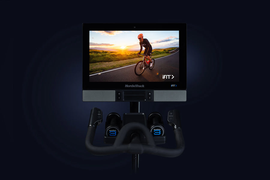 NordicTrack S22i commercial indoor bike with black frame, dual blue-lit resistance knobs, and touchscreen display showing cyc