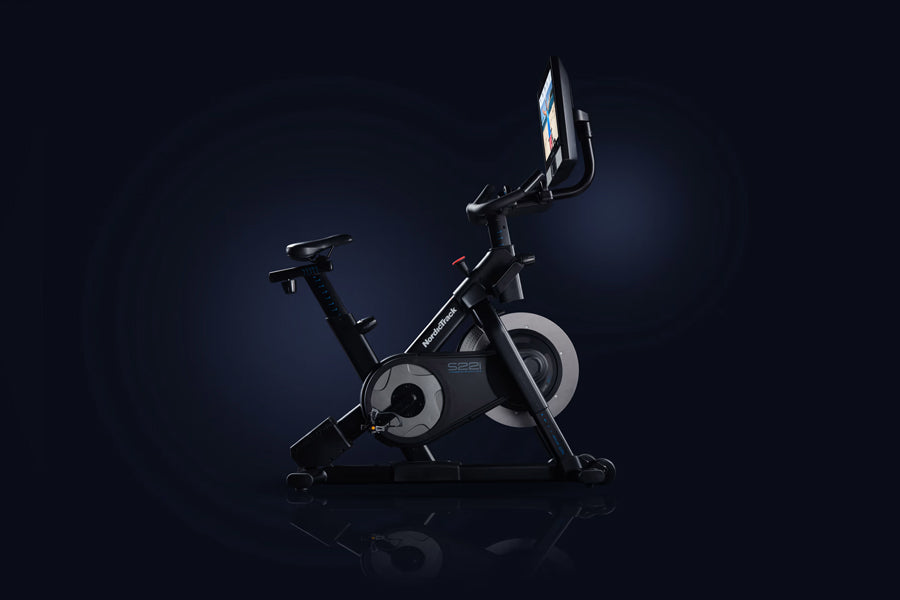 Black NordicTrack S22i stationary exercise bike with digital touchscreen display and gray flywheel on dark background