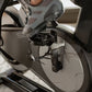 Black and gray stationary exercise bike with digital display and pedals, shown with person's feet in gray sneakers positioned