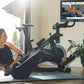 Woman in black tank top and leggings using stationary exercise bike with screen displaying fitness class, indoor home gym set