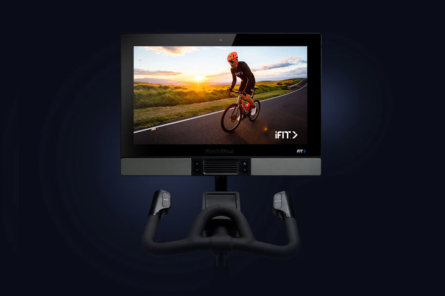 NordicTrack S27i stationary bike with black frame and handlebars, mounted display screen showing cyclist on road at sunset