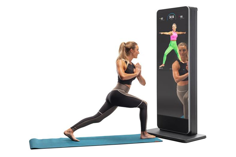 Woman performing lunge exercise on blue mat facing black interactive fitness mirror displaying workout instructor and form gu