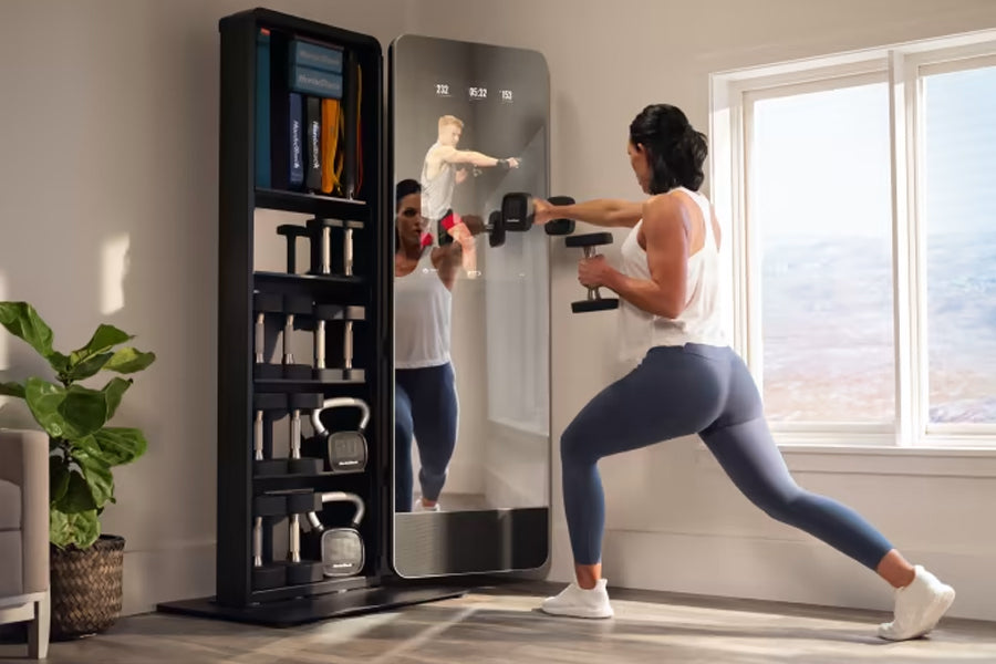 Woman in white tank top and navy leggings using interactive fitness mirror with dumbbell weights, displaying workout instruct