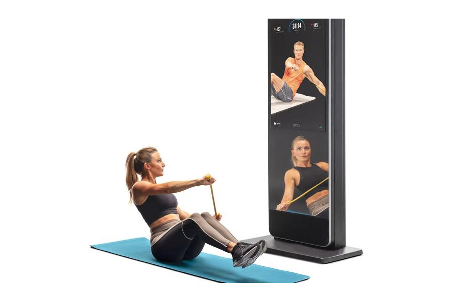 Woman performing seated rowing exercise on blue mat with NordicTrack Vault black mirror displaying workout videos on screen