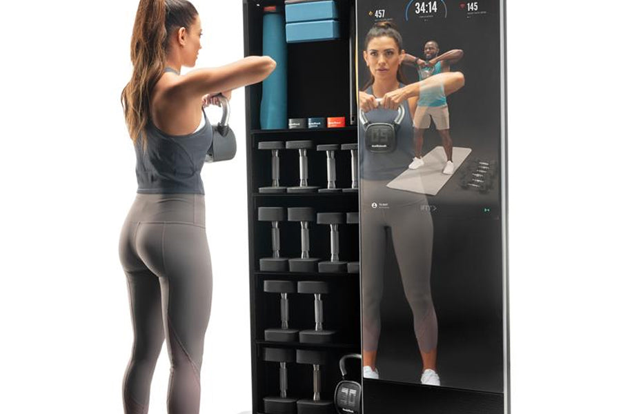 Woman performing dumbbell shoulder press exercise in front of NordicTrack Vault interactive home gym mirror with touchscreen 