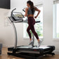 Woman running on NordicTrack X22i treadmill with digital display, wearing gray sports bra and burgundy leggings in bright hom
