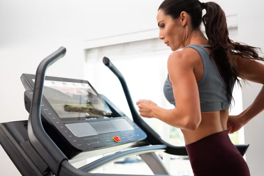 Woman in gray sports bra and burgundy leggings using NordicTrack X22i treadmill with digital display in bright gym setting
