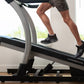 Person running on NordicTrack X22i commercial treadmill with gray frame and black belt, wearing black athletic shoes and gray