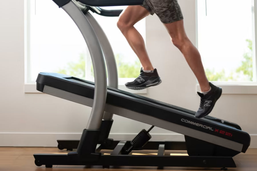 Person running on NordicTrack X22i commercial treadmill with gray frame and black belt, wearing black athletic shoes and gray