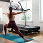 Woman in burgundy leggings and white sports bra using black NordicTrack X22i treadmill with arms outstretched on blue exercis
