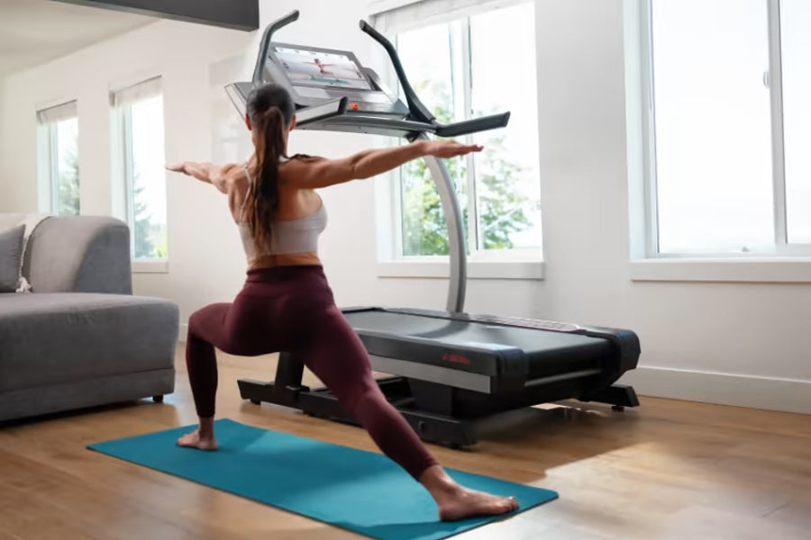 Woman in burgundy leggings and white sports bra using black NordicTrack X22i treadmill with arms outstretched on blue exercis