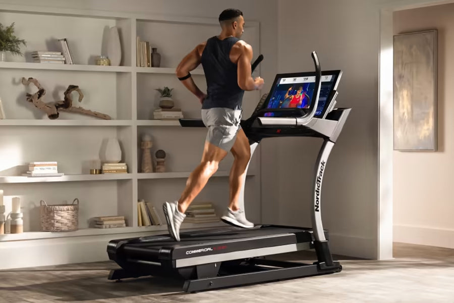 Man running on black and white NordicTrack X32i commercial treadmill with dual touchscreen displays in modern home gym