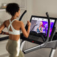 Woman using black and silver NordicTrack X32i treadmill with interactive screen display, wearing white sports bra and beige l