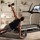 Man performing plank with dumbbell on black mat in front of NordicTrack X32i treadmill with touchscreen display in home gym