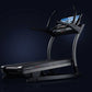Black and silver commercial treadmill with digital display screen, curved handrails, and wide running deck on dark background