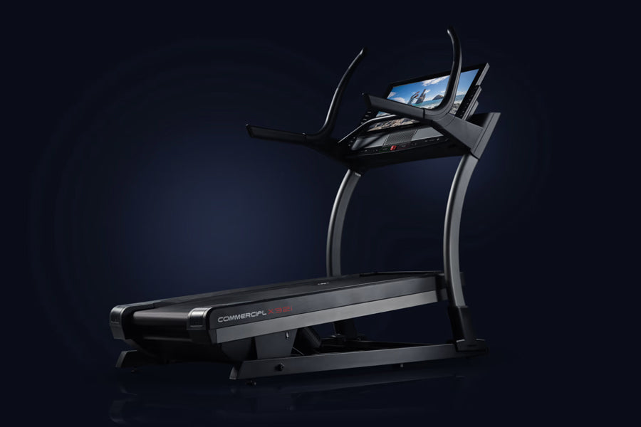 Black and silver commercial treadmill with digital display screen, curved handrails, and wide running deck on dark background