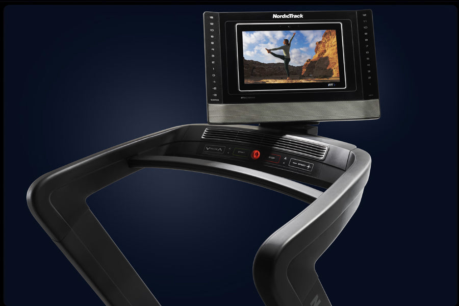 NordicTrack 1750 commercial treadmill with black and silver frame, digital display console showing fitness video, on dark blu