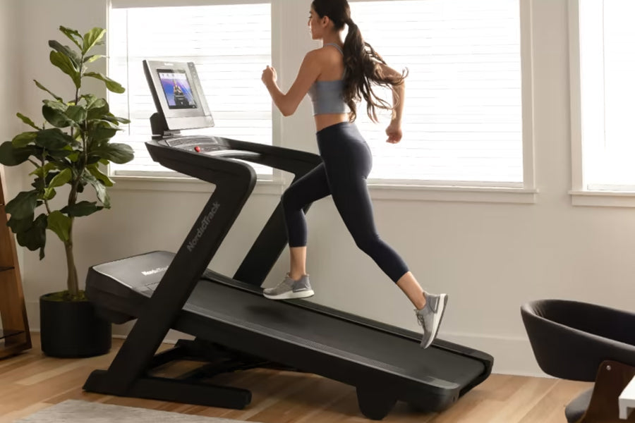 Woman running on black NordicTrack treadmill with digital display in bright home gym with potted plant